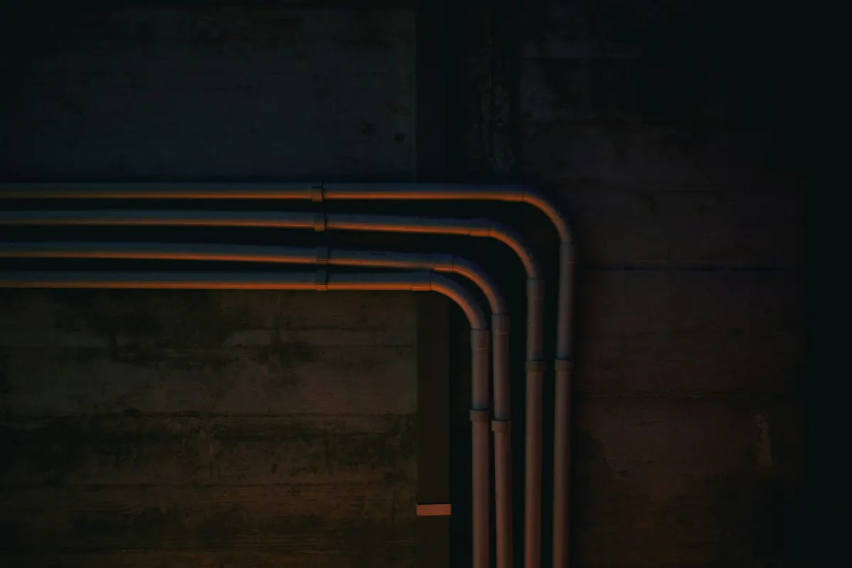 Four parallel pipes bending around the corner of a dark concrete wall