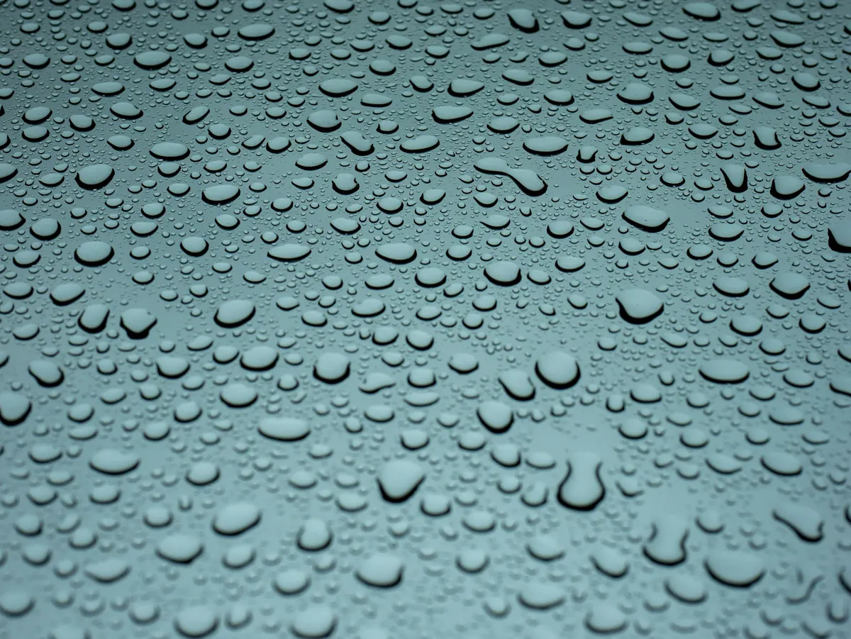 Beads of water gathered on a blue-grey glass surface