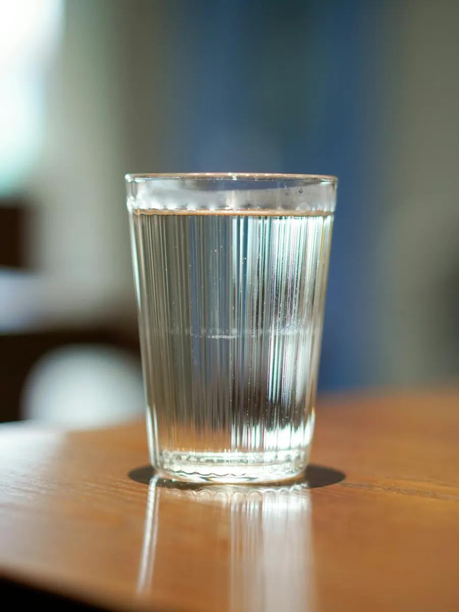 A ribbed glass of clear water on a sunlit wooden table
