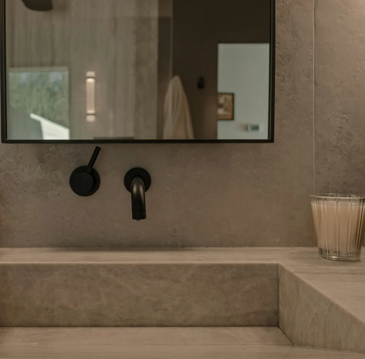 Matte black wall-mounted faucet and handle above a carved stone basin