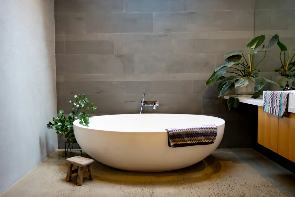 Freestanding stone-white tub with a wall-mounted chrome filler against grey stone tile